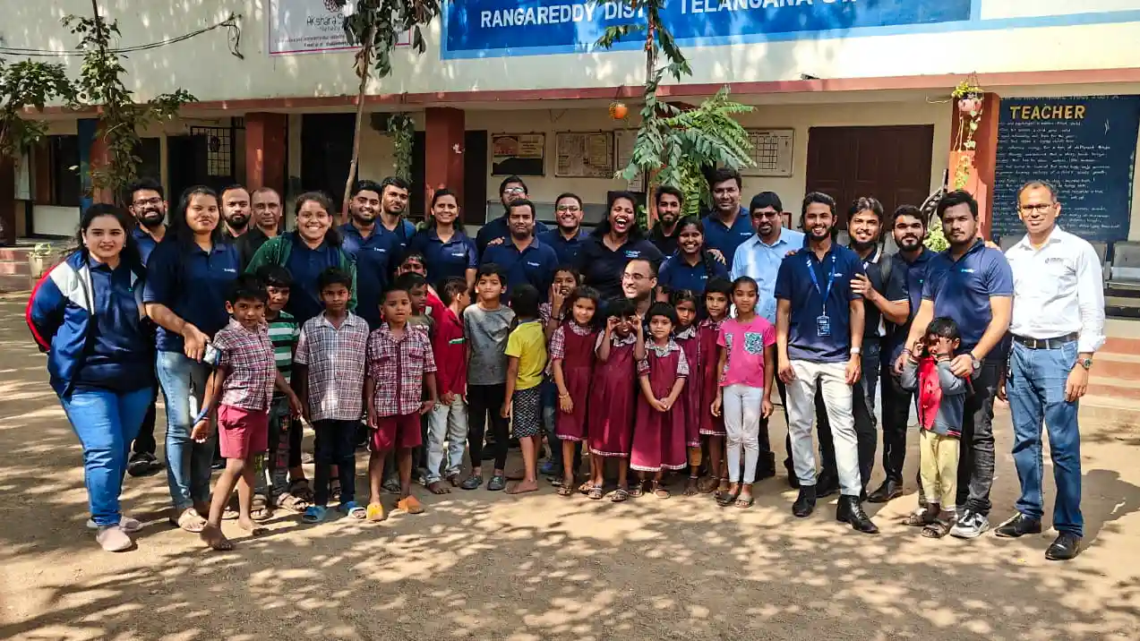 A smiling man shakes the hands of children who crowd around him in a classroom.|Children line up for an eye screening program at a school in India.||