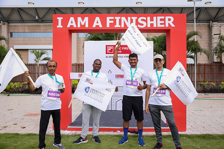 A blue banner with the words "Running to give the Gift of Sight" across it.|A group of men stand in matching t-shirts with medals around their necks in front of a starting gate.